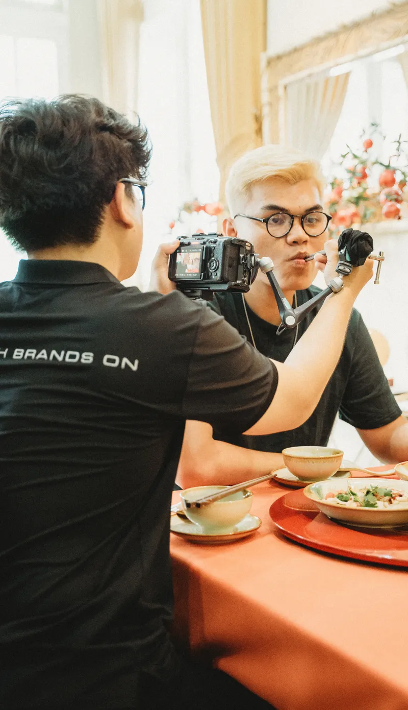 Operator filming a close-up of the artist tasting a dish at the table