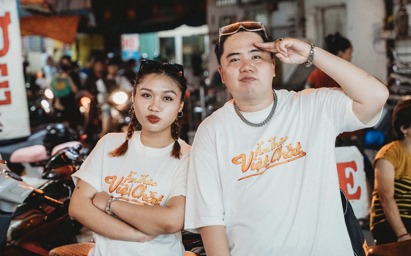 Rap duo in Ẩm Thực Việt Chất tees posing at a night street-food market