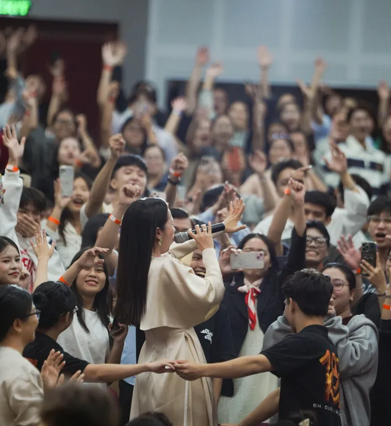 Singer performing among a cheering student audience with raised hands